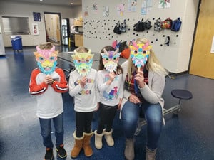 three students and one staff member wearing homemade dragon masks